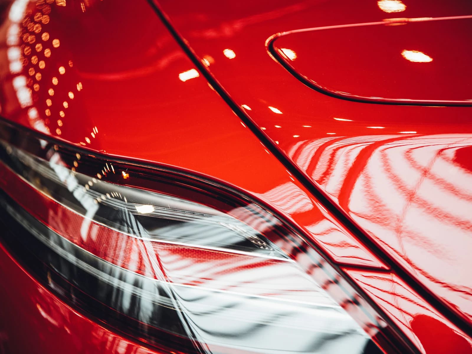Hard-edged highlights reflected in deep red paint, holding their shape as they bend over the panel crease
