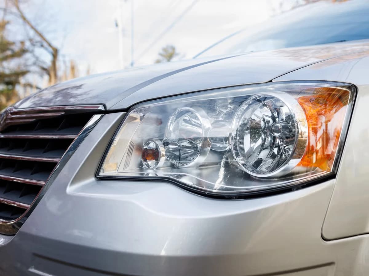 A fully clear headlight lens on a silver car, the reflector and projector sharp behind it