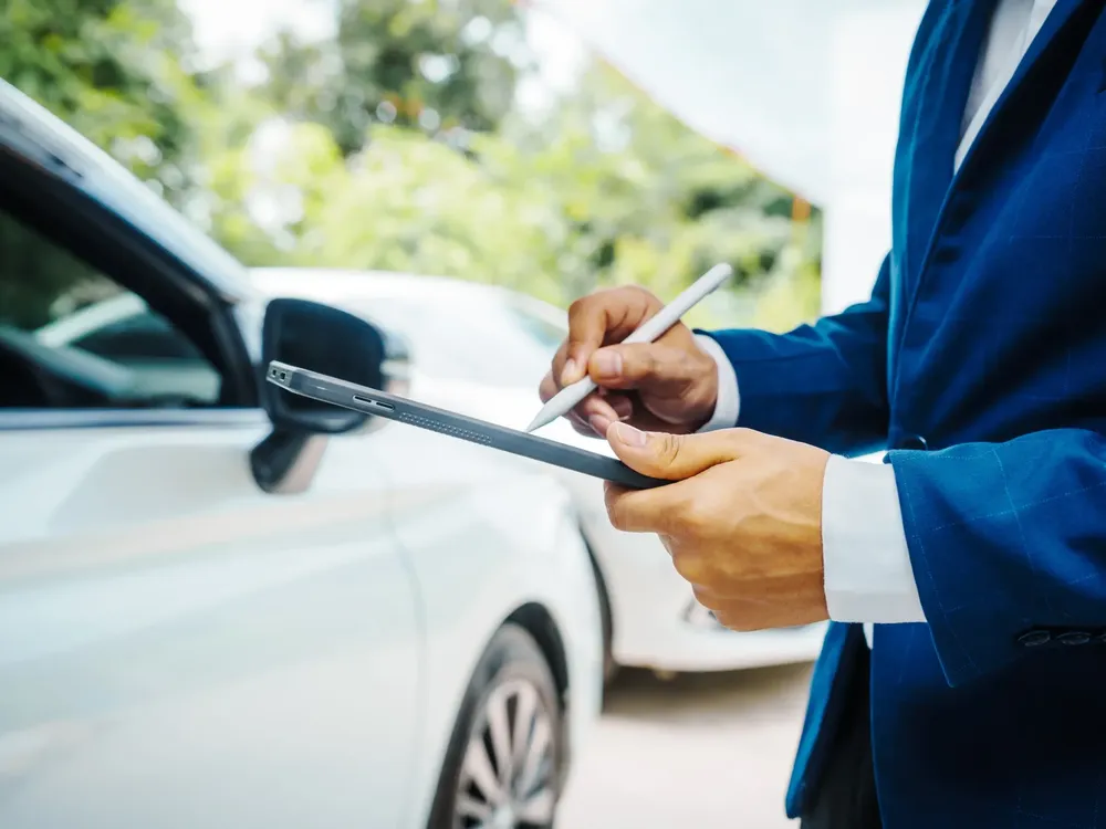 A person in a business suit making notes on a tablet beside a white car