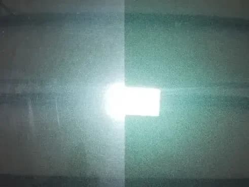 A dark green car panel under a work light, the left half clouded with fine swirl marks and the right half polished clear