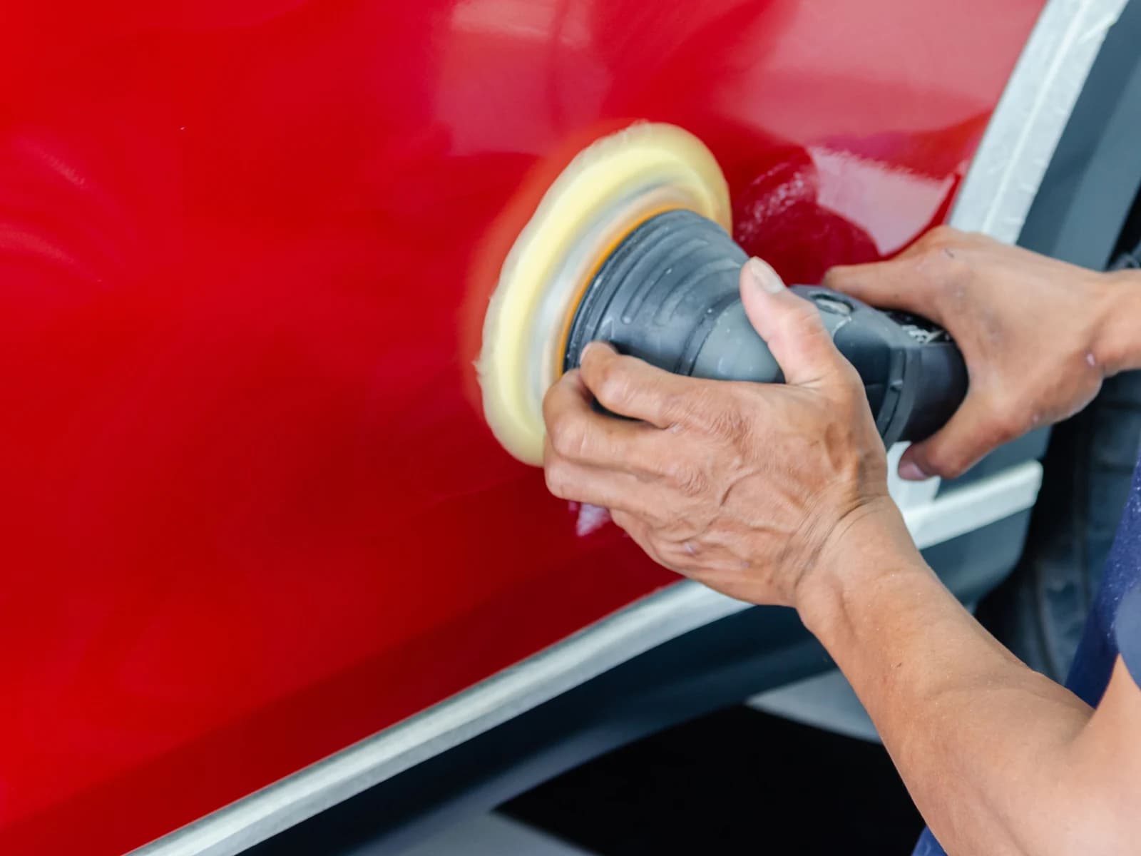 A polisher working a small area of a red door, the surrounding panel untouched