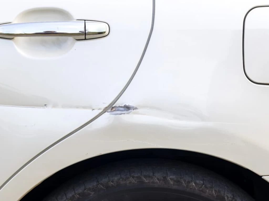 A deep gouge through the paint of a white door, the panel creased around it — past what polishing can fix